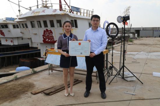 海鮮電商張夢(mèng)琴與幫辦員手持食品經(jīng)營(yíng)許可證合影。贛榆區(qū)委宣傳部供圖